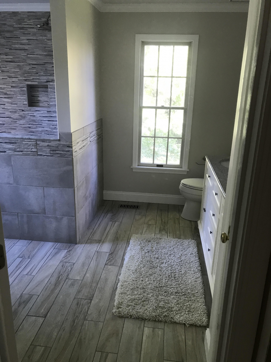 Remodeled bathroom with stacked stone shower surround and wood-look tile floor