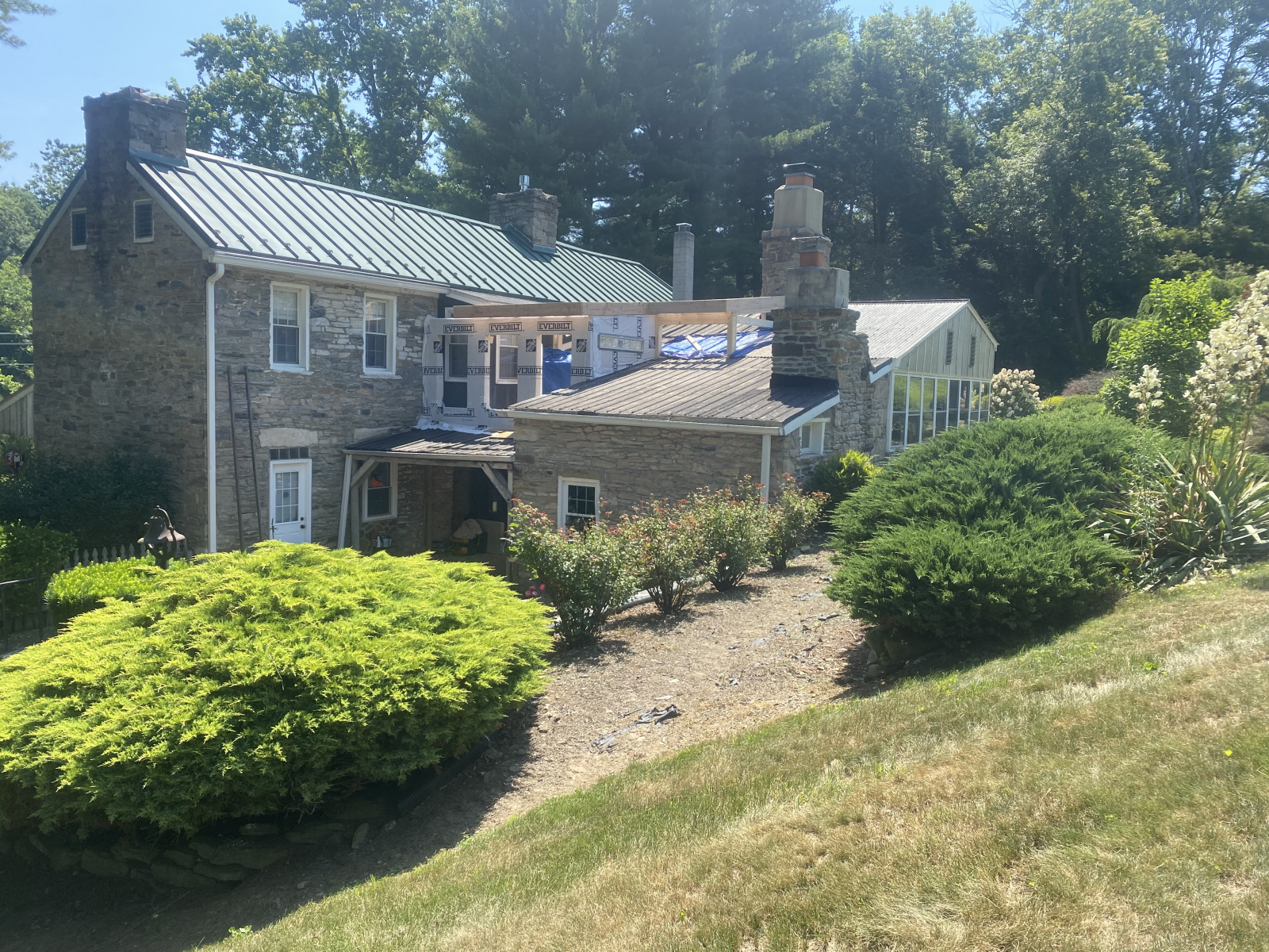 Second-floor addition in progress: framing and weather wrap over existing stone farmhouse