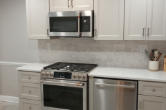 White shaker kitchen with quartz counters, gas range, and stone backsplash