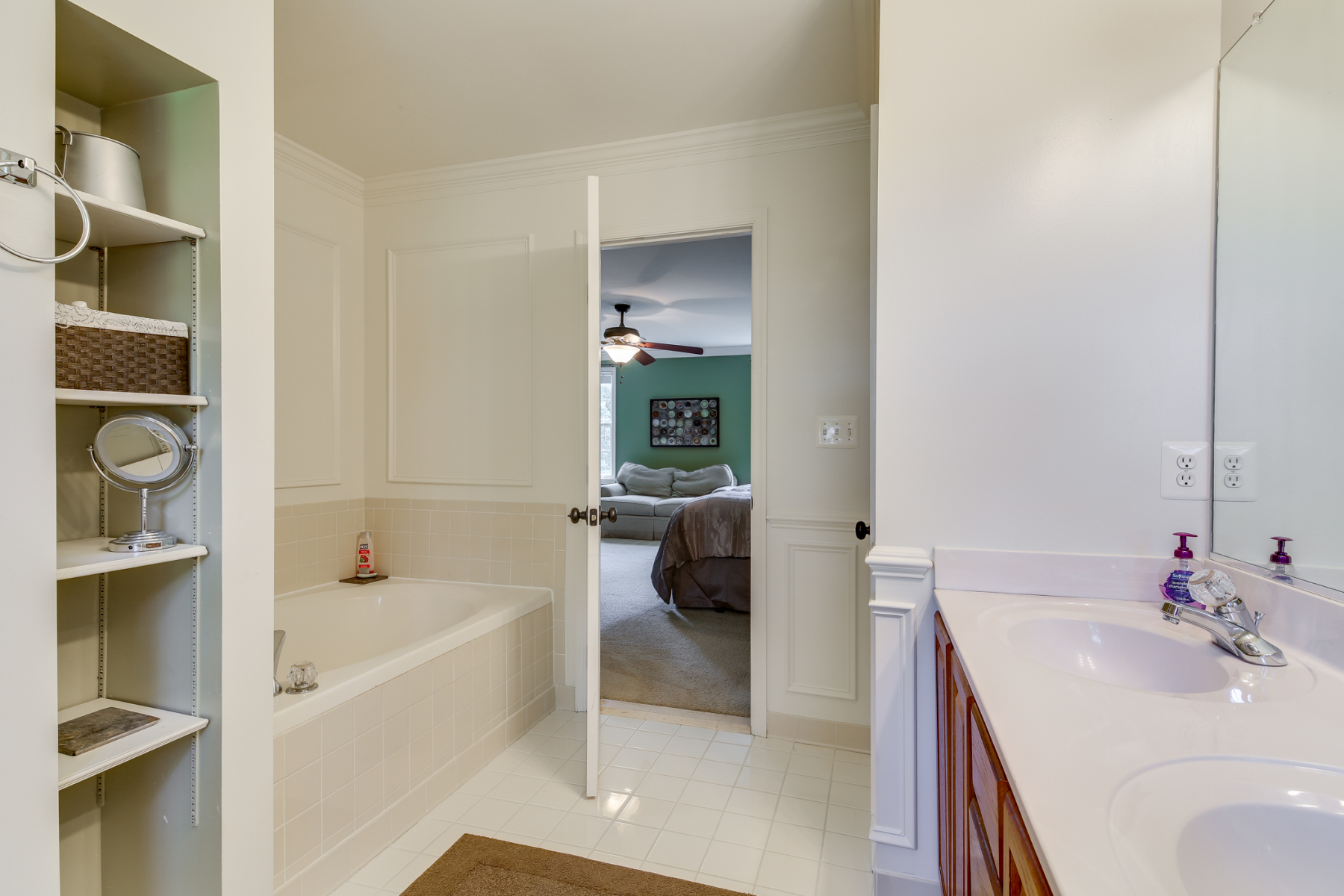 Master bathroom before remodel with built-in shelving and white tile tub