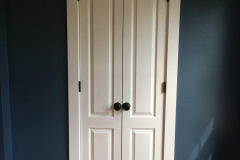 Custom paneled interior door with vintage hardware against deep blue wall