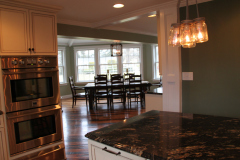 Custom kitchen with built-in double ovens and granite peninsula opening to dining