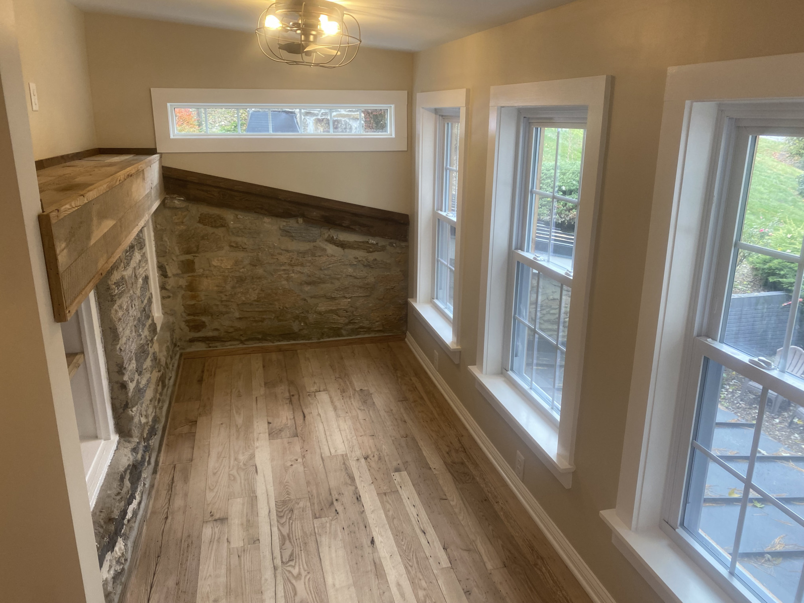 Interior of finished second-floor addition with exposed stone wall, reclaimed wood trim, and new hardwood floors