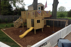 Custom backyard play fort with slide, flags, and mulched play area